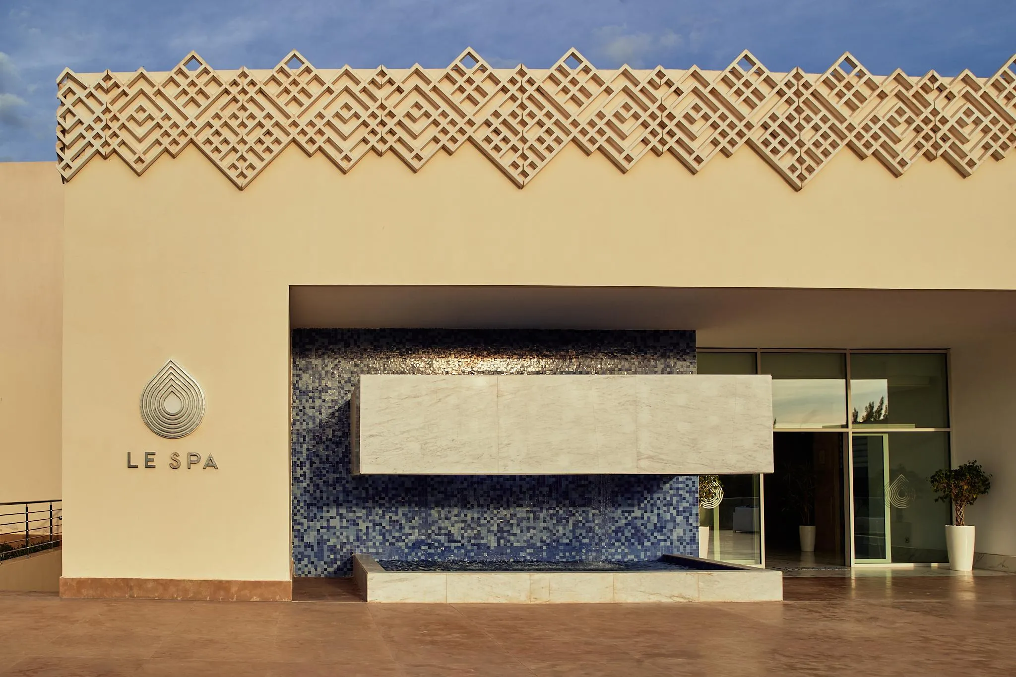 Façade d'un spa avec un mur en mosaïque bleue, une table en pierre et des plantes en pot