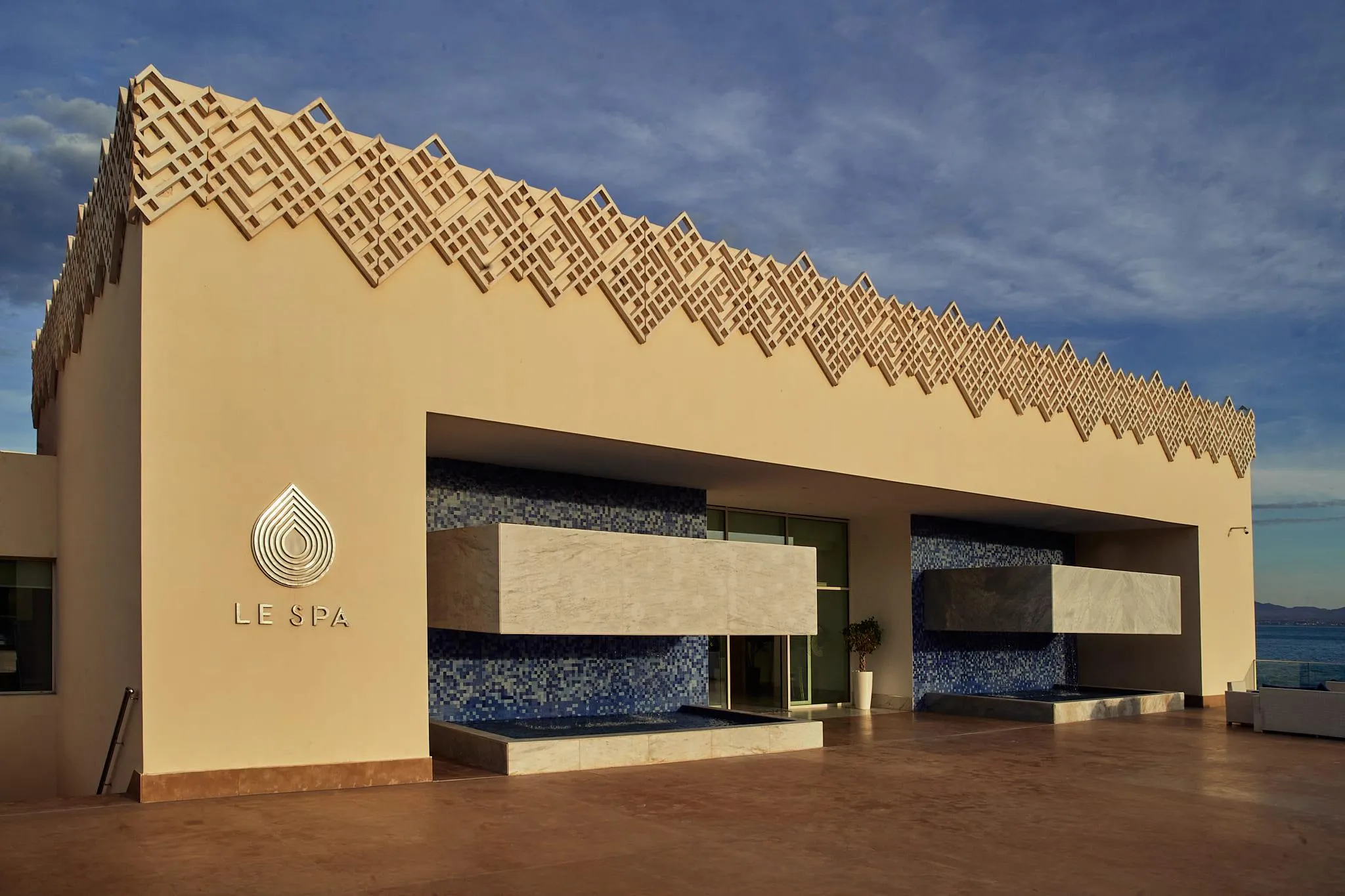 Fachada de un edificio llamado "LE SPA" con decoración mural en mosaico azul y motivos geométricos en relieve en el techo