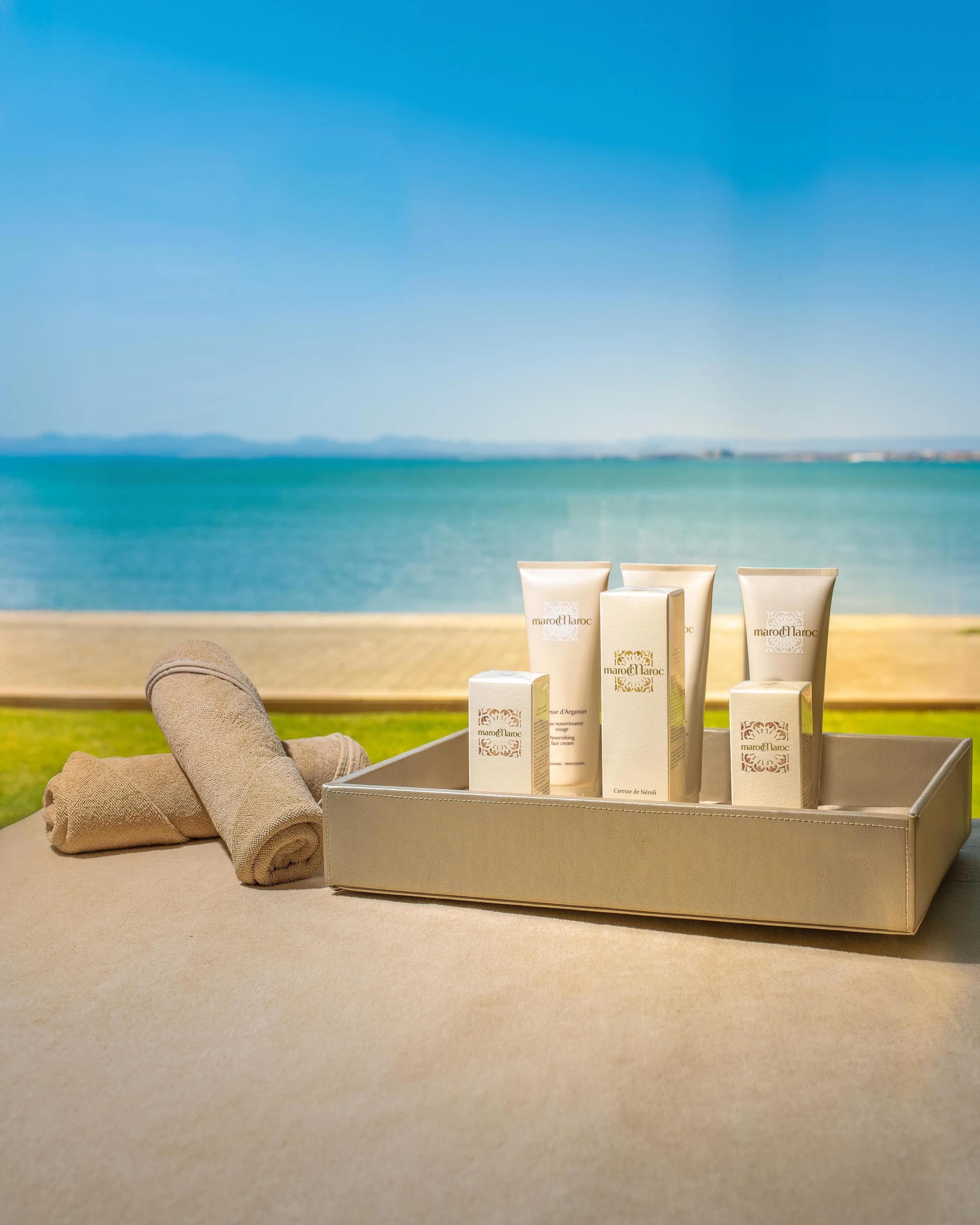 A tray with cosmetic products and fabric towels in front of a beach and the sea