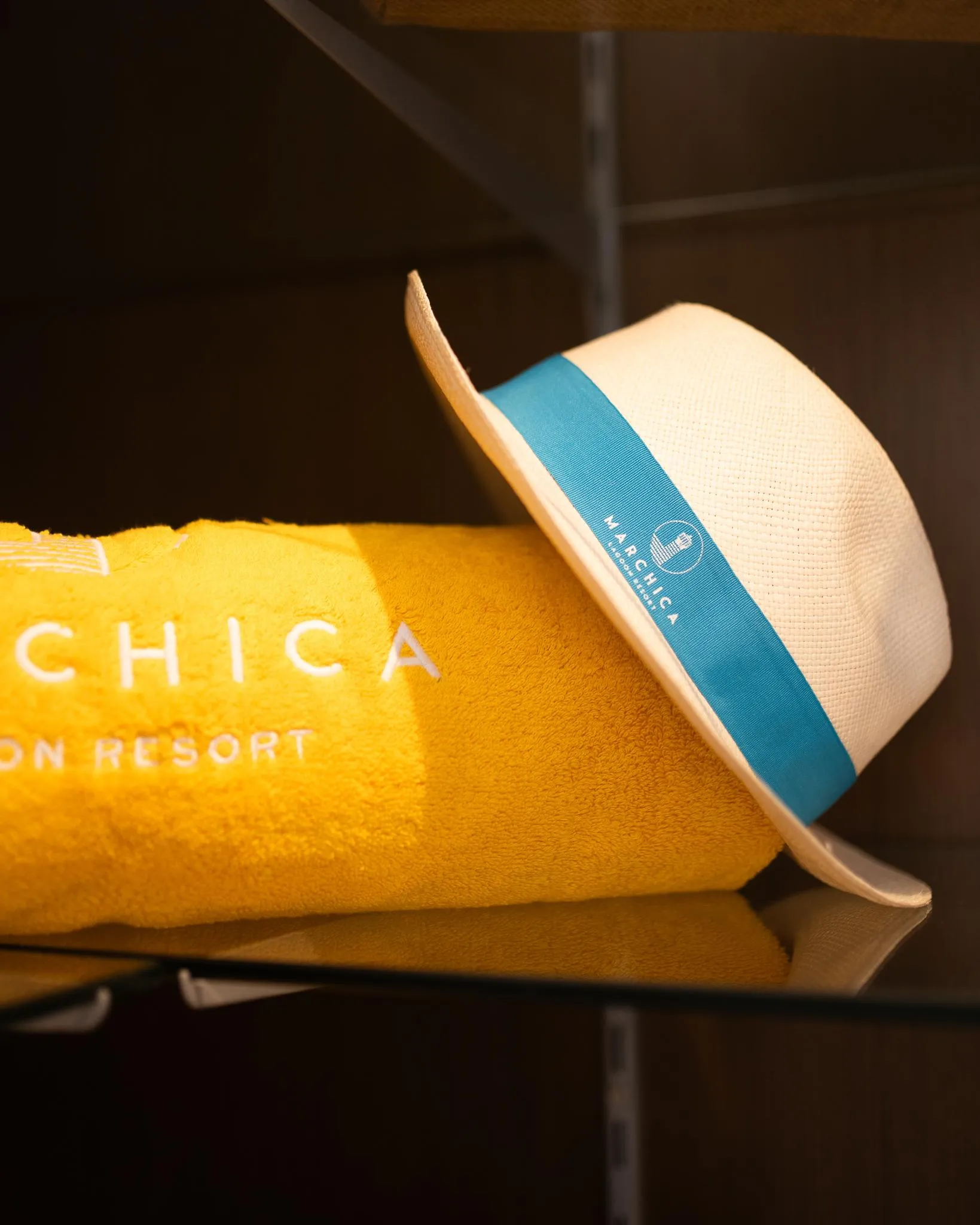 A white straw hat with a blue band bearing the inscription "Archipiélago" placed on a yellow object with the inscriptions "CHICA" and "ON RESORT"