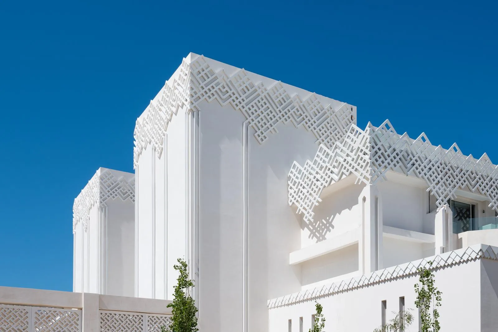 White building with geometric relief patterns on the facade and roof, under a clear blue sky