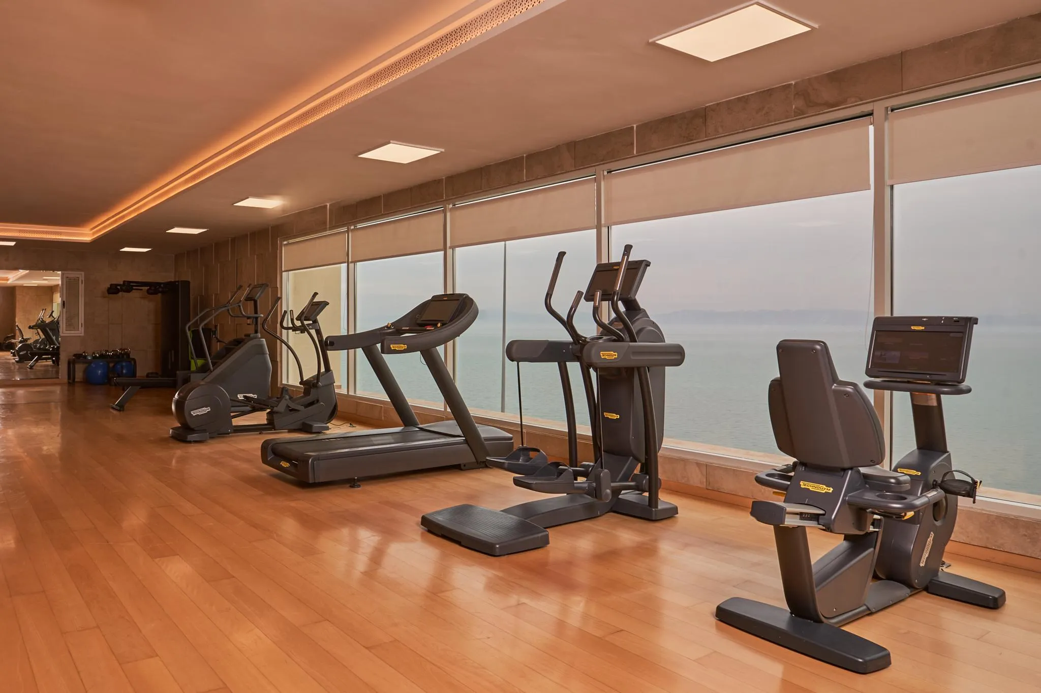 Salle de sport avec plusieurs appareils de fitness devant une grande fenêtre offrant une vue sur la mer