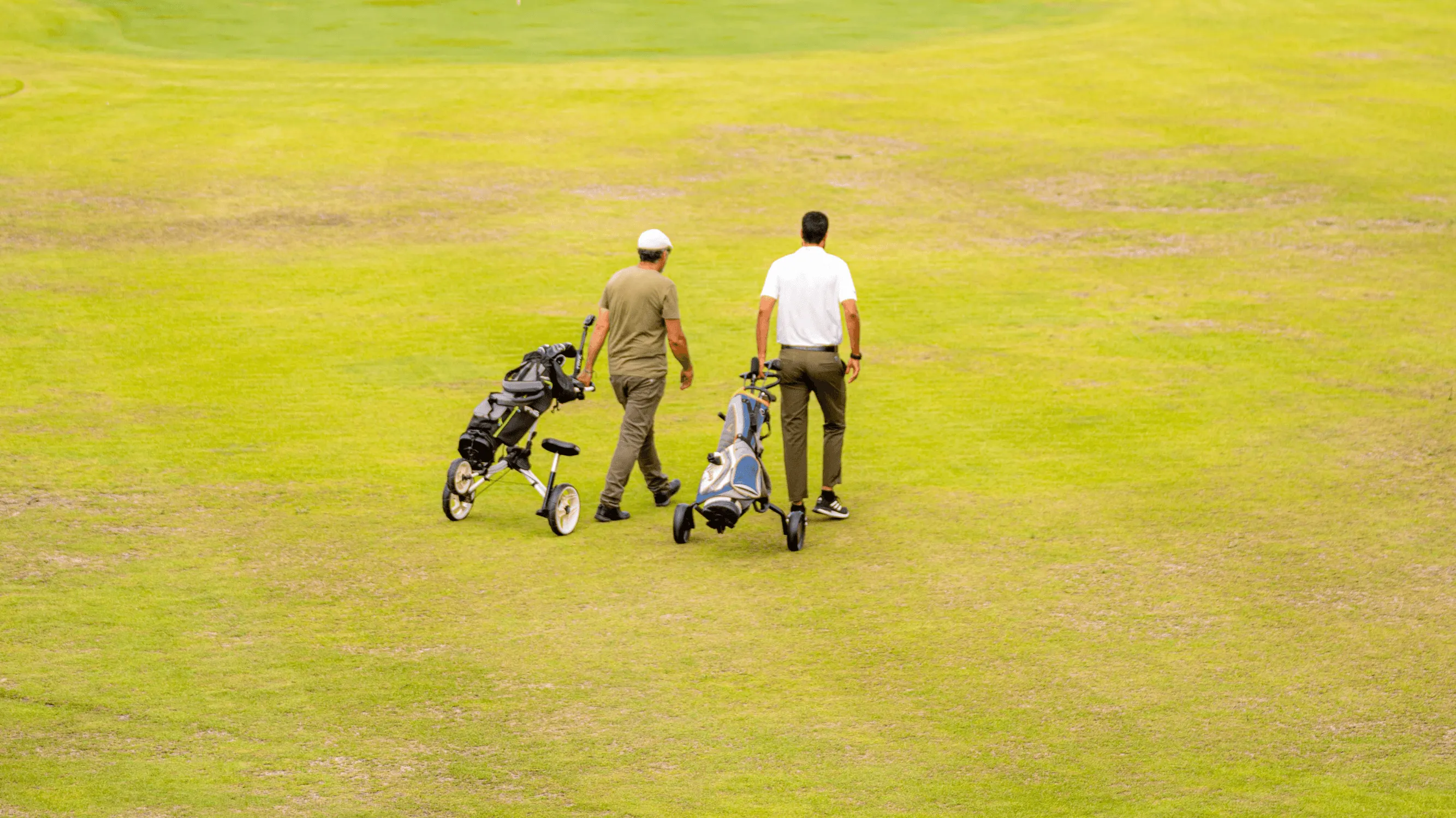 Two people are walking on a golf course pushing golf club carts.