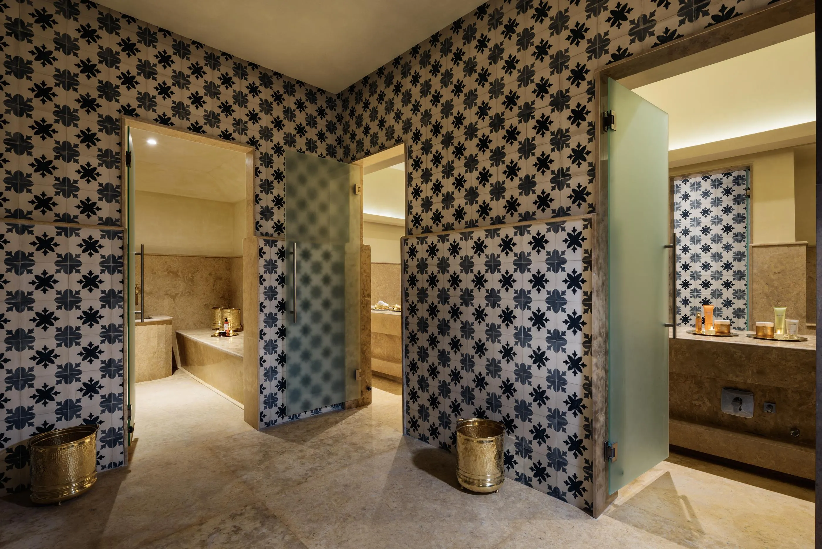Luxurious bathroom with floral-patterned blue and white wall tiles, stone basins, and gold metal accessories.