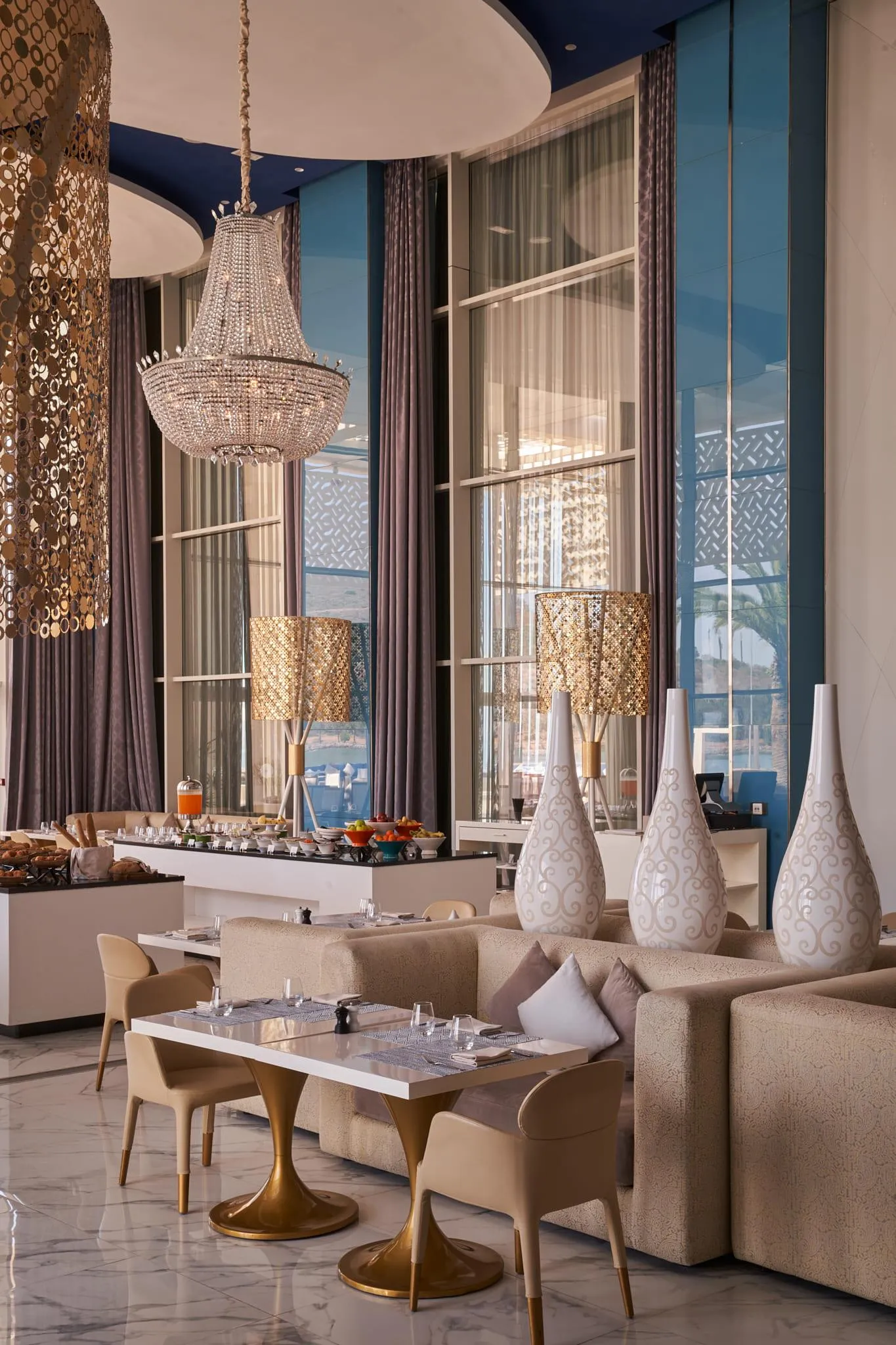 Salle à manger élégante avec tables, chaises, canapés, lustres et vue sur la mer à travers de grandes fenêtres