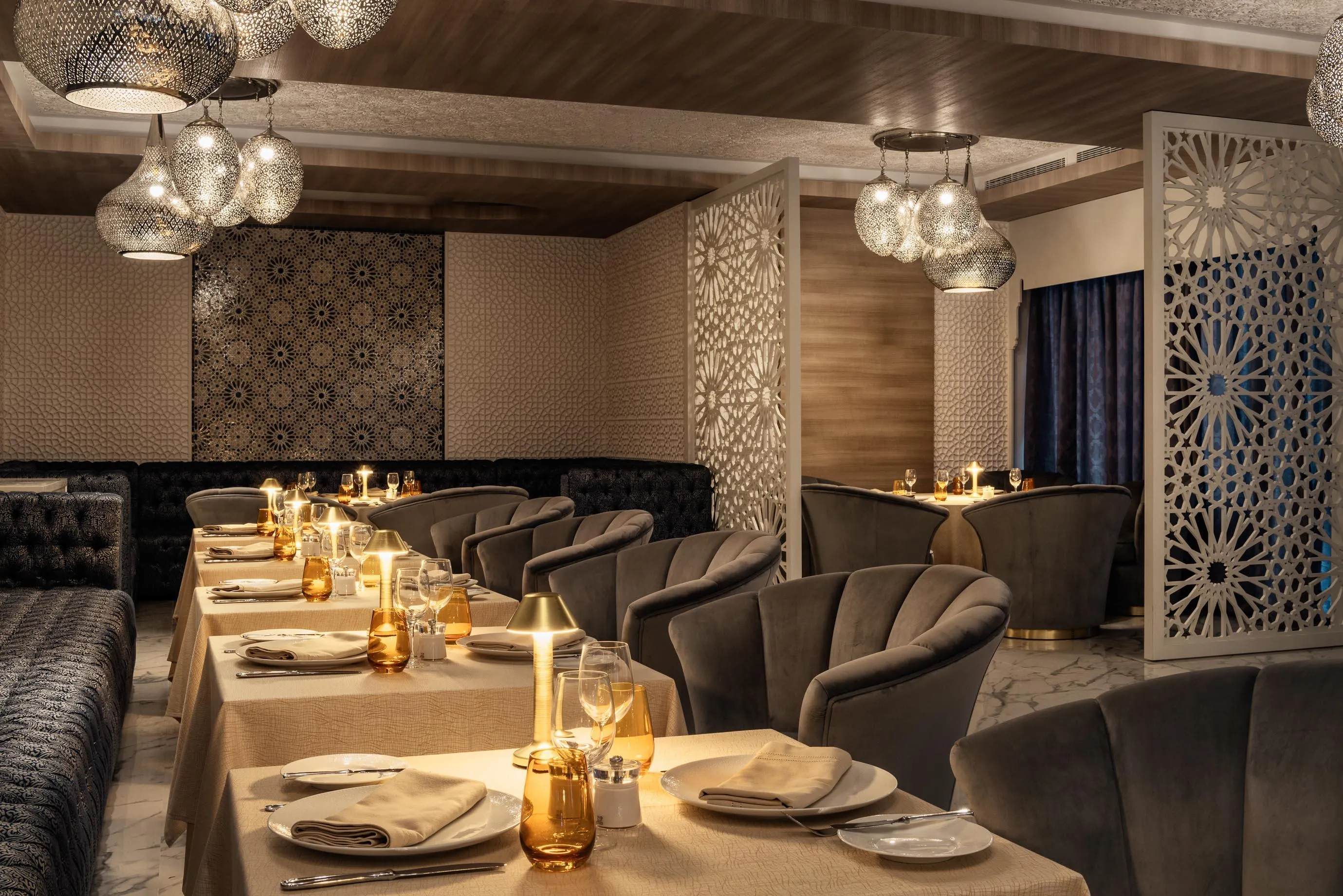 Salle à manger élégante avec tables dressées, chaises rembourrées et décorations murales géométriques