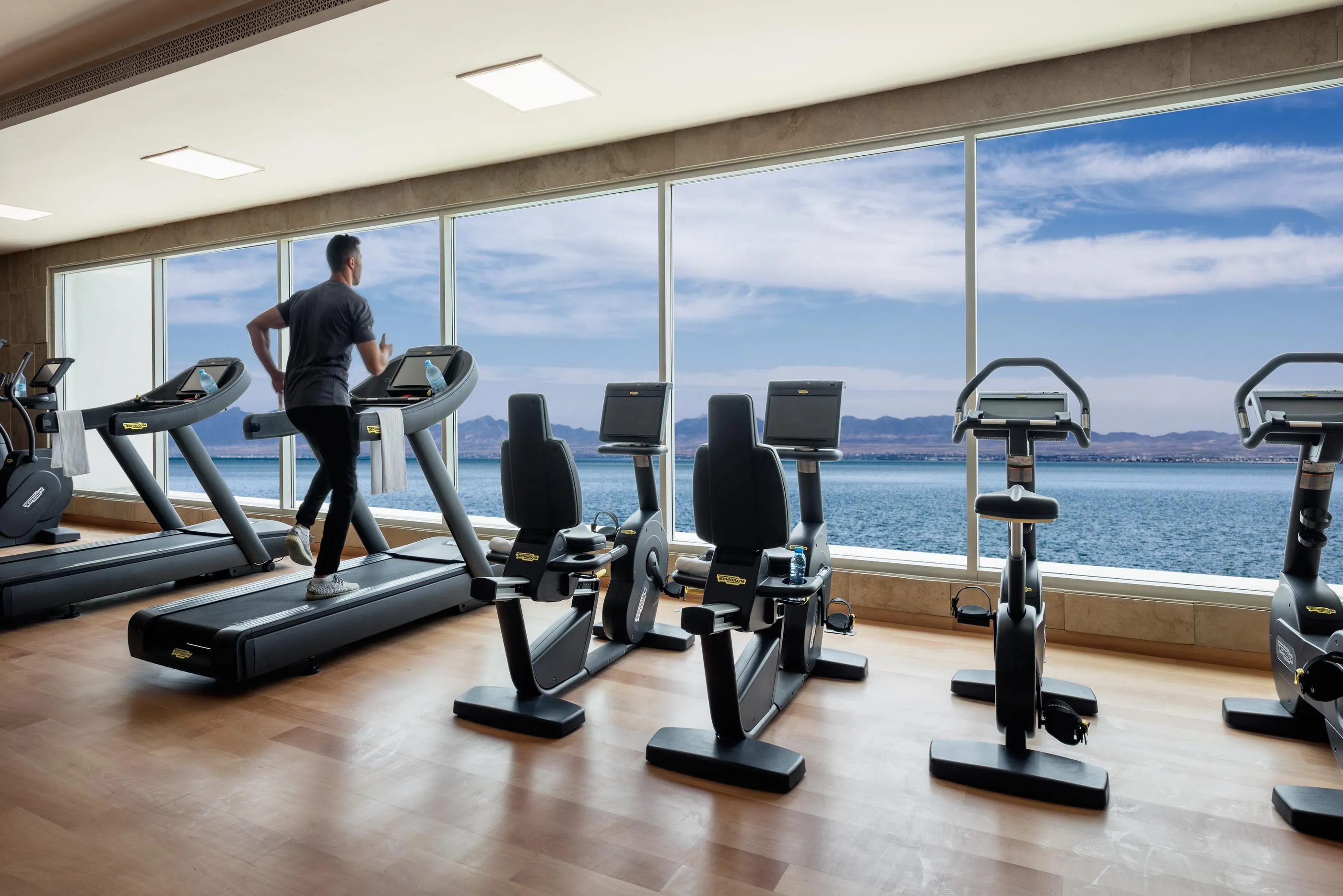 Une personne marche sur un tapis de course dans une salle de sport avec vue sur la mer