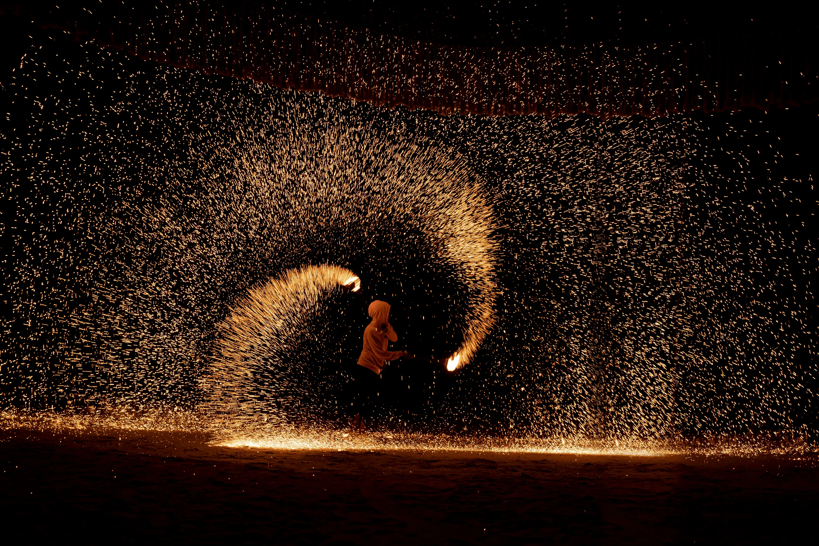 A person throws sparks in an arc on a nighttime beach.