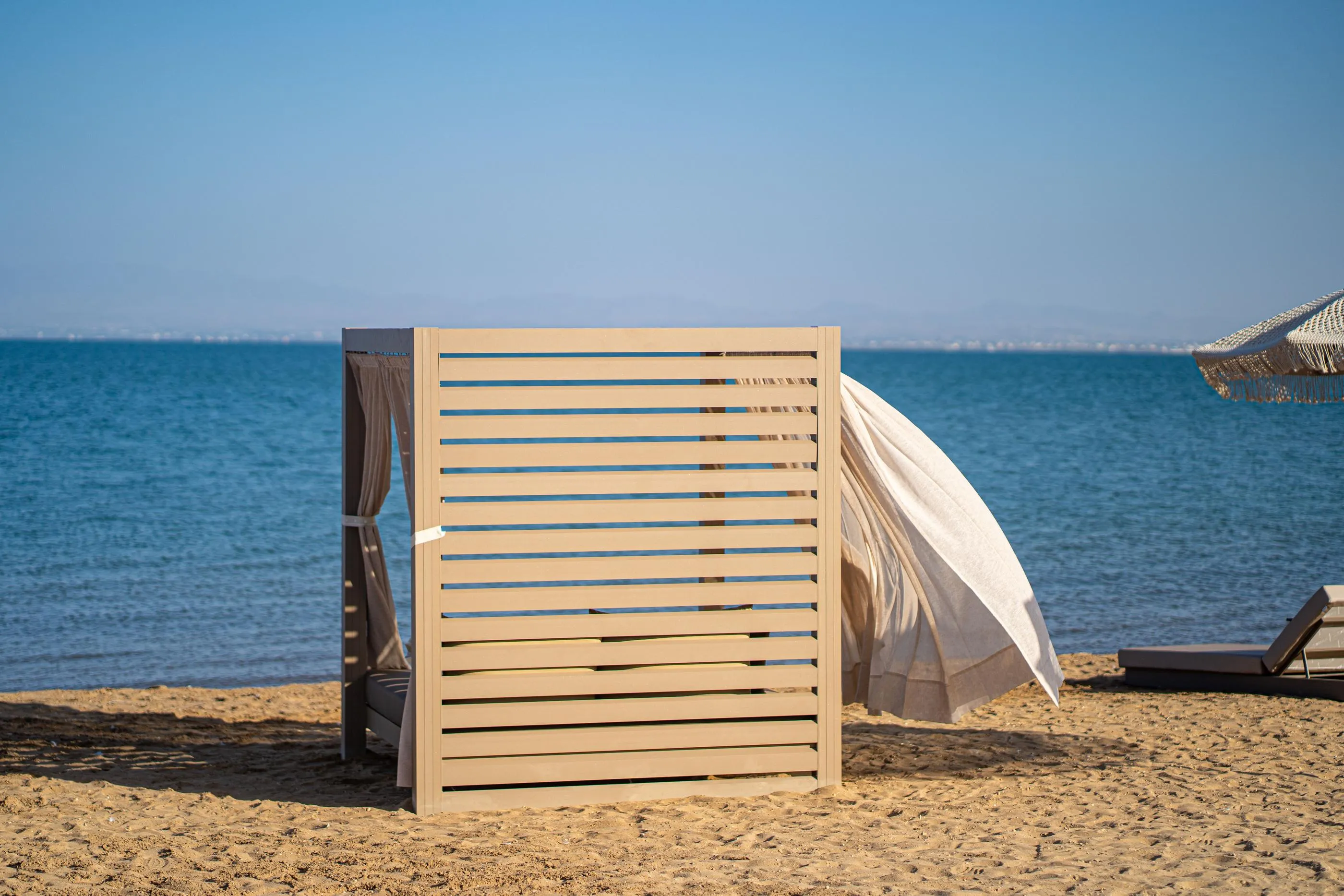 Wooden cabin on a sandy beach with a white canvas and a view of the blue sea