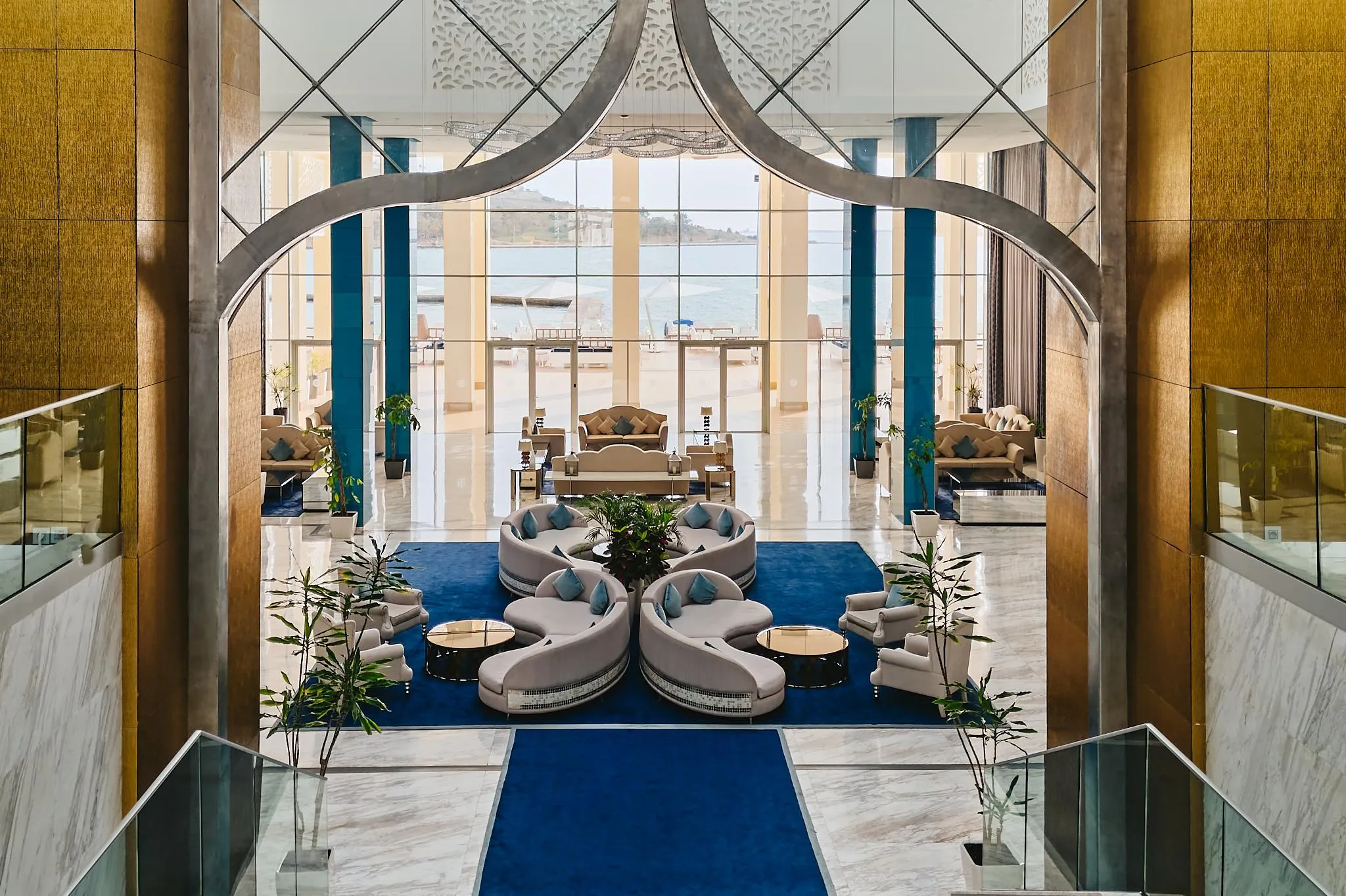 Un espacio interior lujoso con sofás modulares, plantas verdes y una vista al mar a través de grandes ventanales.