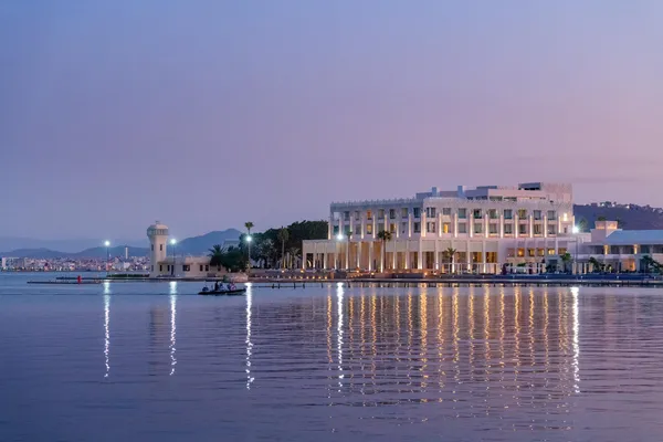 Un bâtiment moderne éclairé en bord de mer avec un petit bateau sur l'eau au coucher du soleil