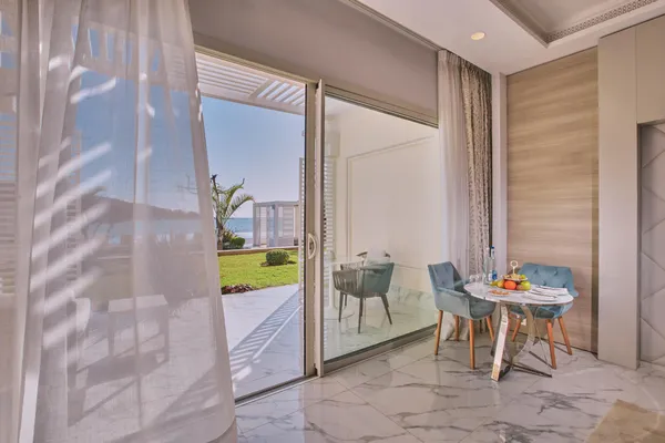 A table with fruits and glasses is set up near a glass door open to a balcony with a sea view.