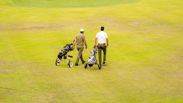Deux personnes marchent sur un terrain de golf en poussant des chariots de clubs