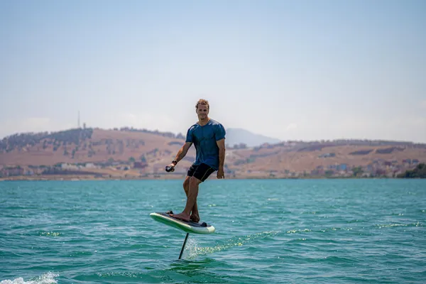Un hombre de pie sobre una tabla de paddle en una extensión de agua con colinas de fondo
