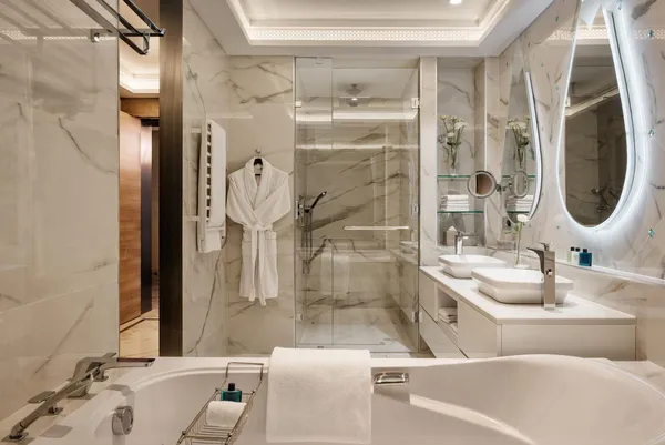 Luxurious bathroom with bathtub, glass shower, double sink, and illuminated round mirror