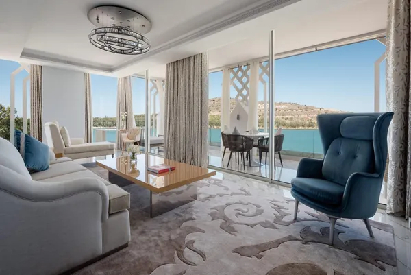 Modern living room with sofa, armchair, and coffee table, opening onto a terrace with a view of a pool and hills.