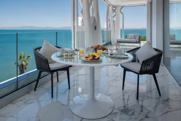A table with breakfast is set up on a balcony with a sea view.