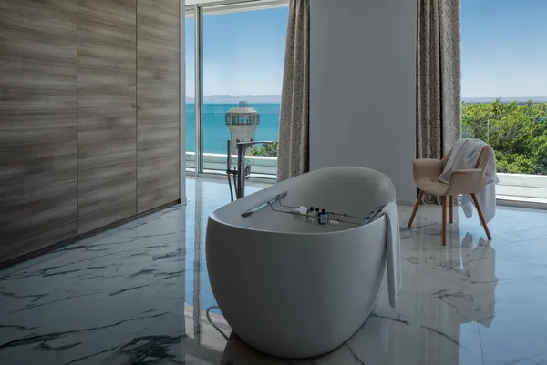 White bathtub with towels placed on it, located in a room with a sea view and an armchair covered with a towel.